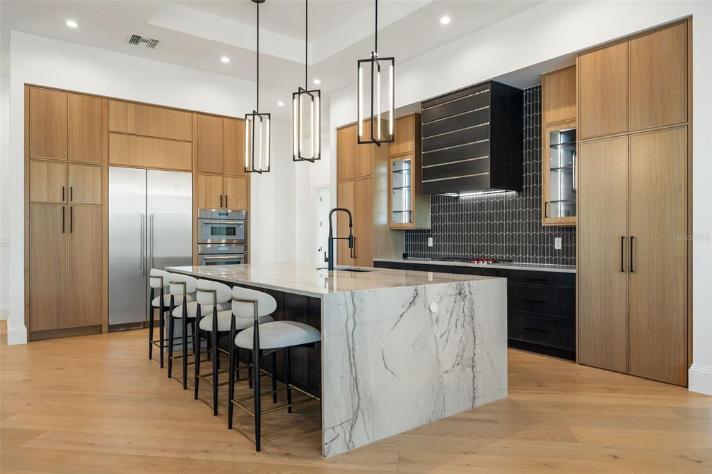 A modern kitchen features light wood cabinetry, a large marble island, and black accent details — 15850 HAMPTON VIEW COURT, FORT MYERS, FL