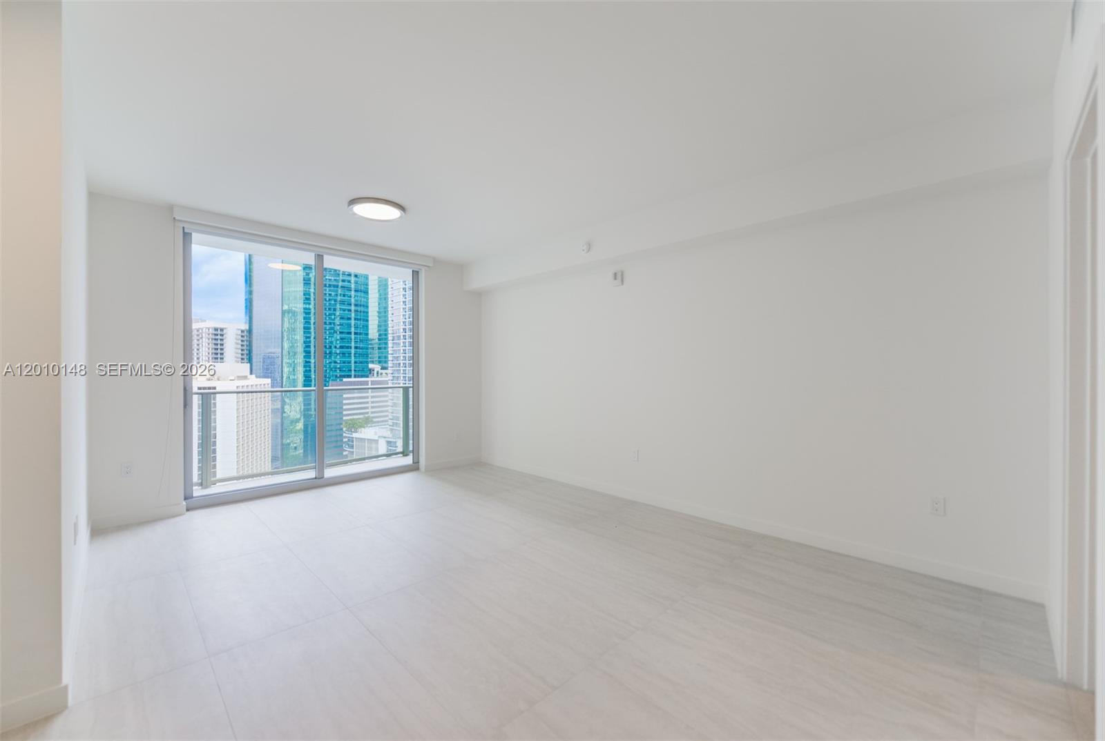 An empty room with white walls, light-colored tile flooring, and a sliding glass balcony door — 77 SE 5 Street # 2604, Miami FL 33131, MIAMI, FL