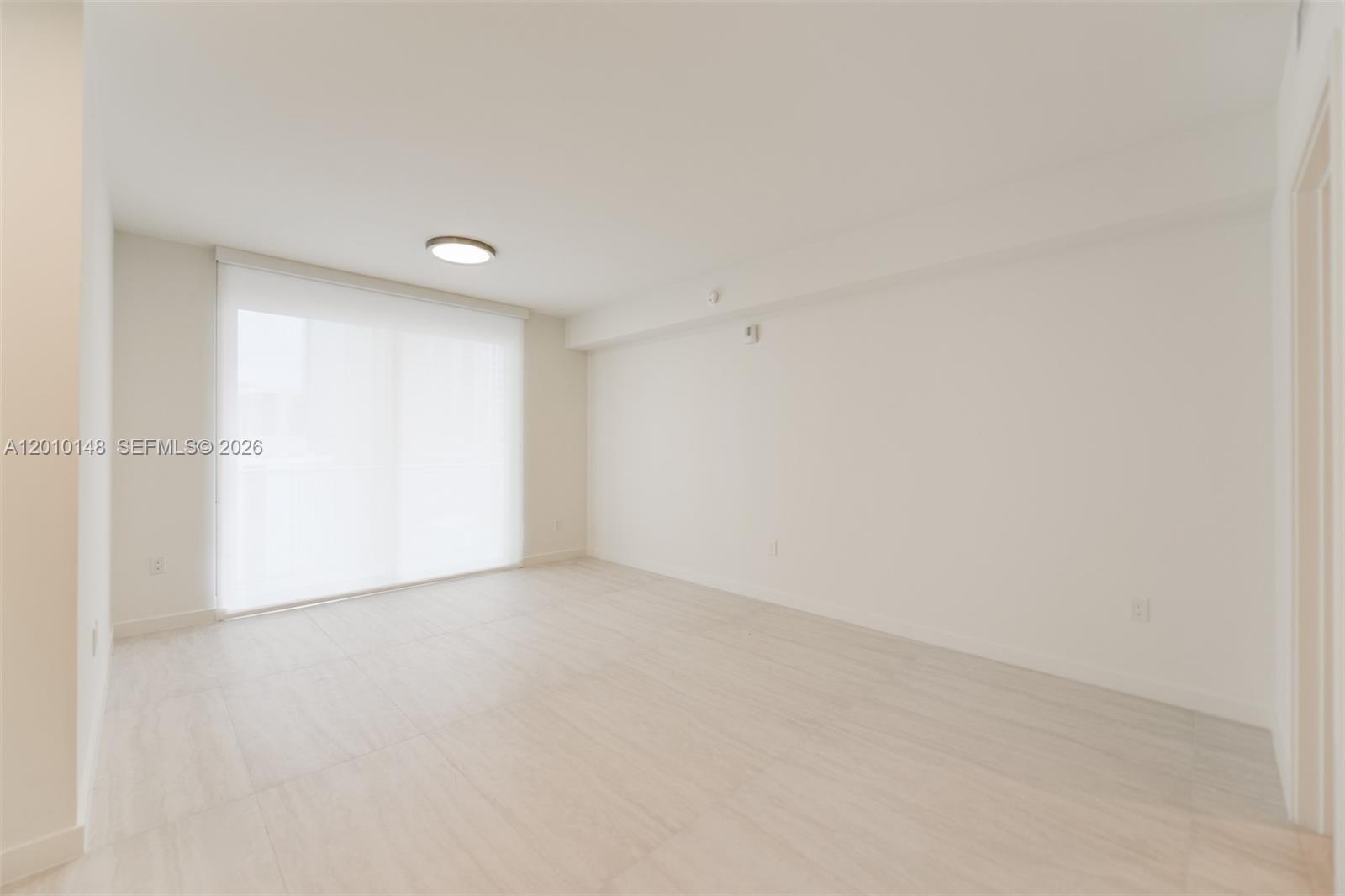 An empty room features light-colored tile flooring, white walls, and a large sliding glass door — 77 SE 5 Street # 2604, Miami FL 33131, MIAMI, FL