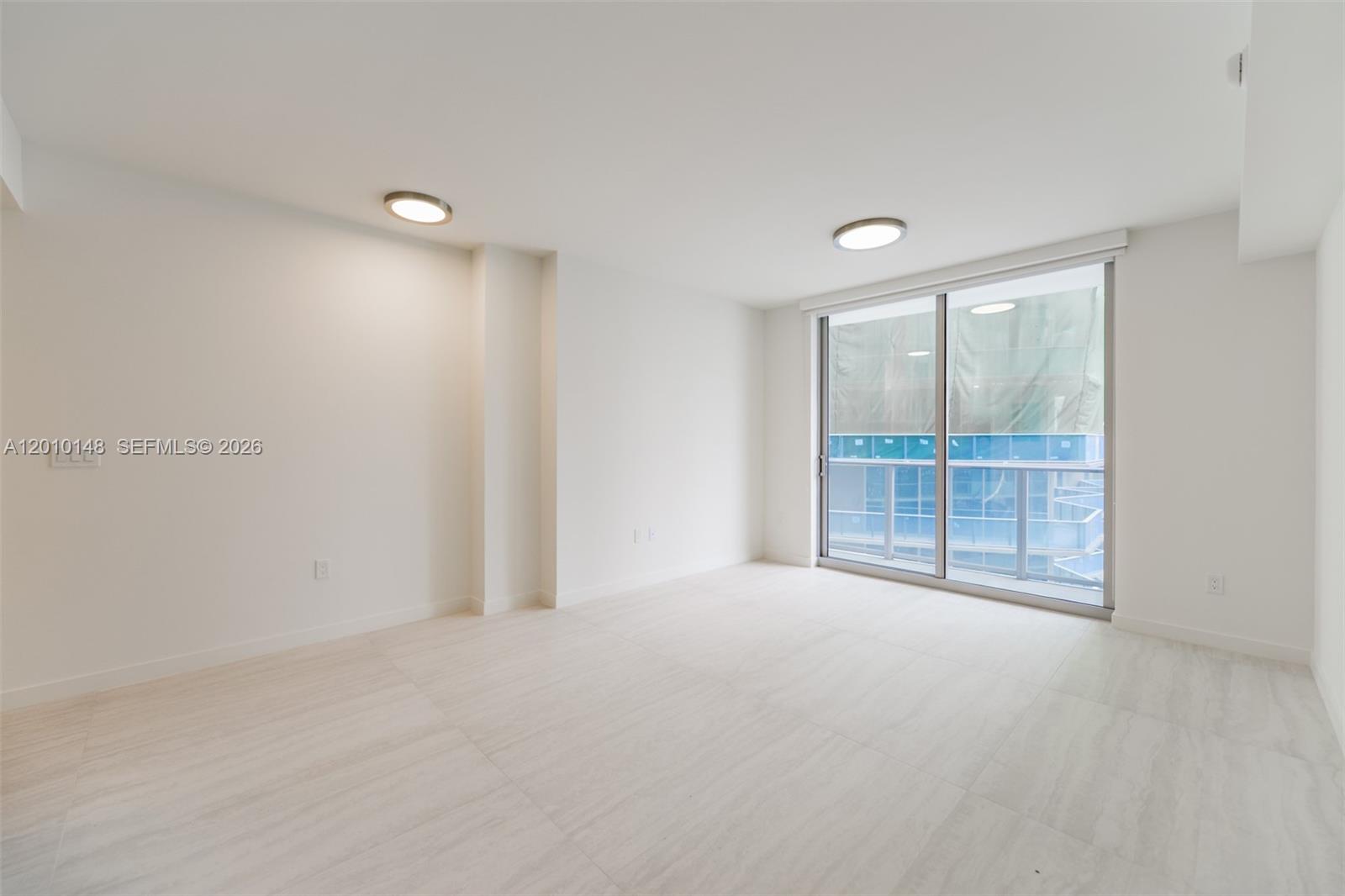 An empty room with white walls, light tile flooring, two ceiling lights, and a balcony — 77 SE 5 Street # 2604, Miami FL 33131, MIAMI, FL