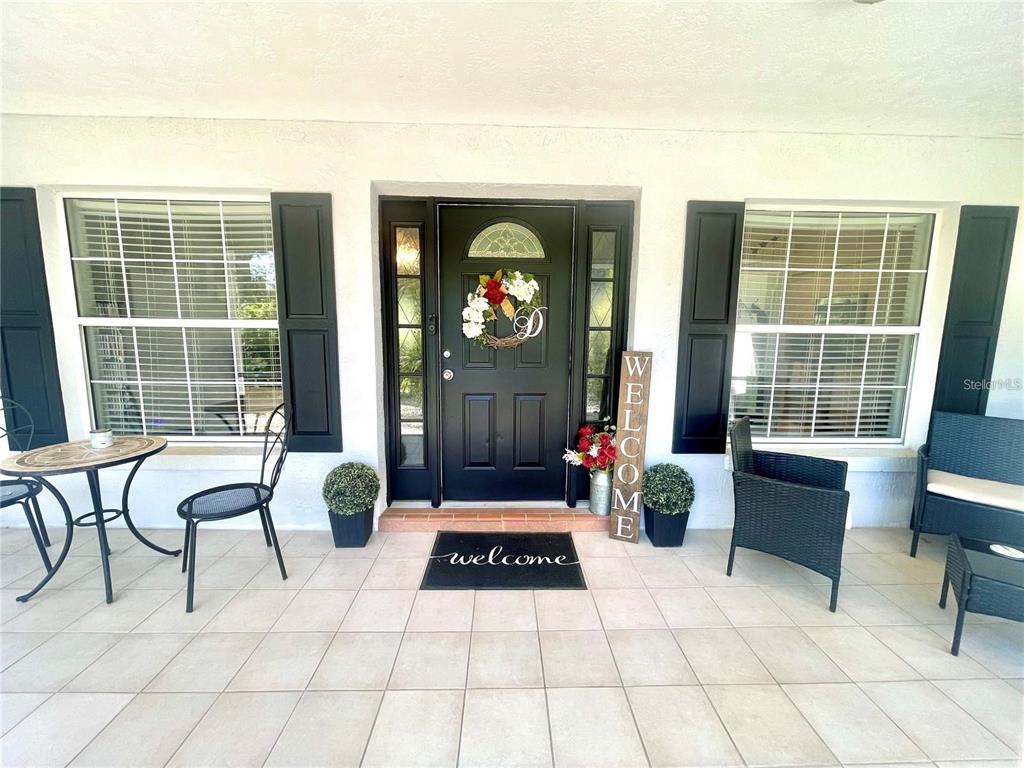 A covered front porch features a black door, tiled flooring, and outdoor seating furniture — 4353 W PINE RIDGE BOULEVARD, BEVERLY HILLS, FL