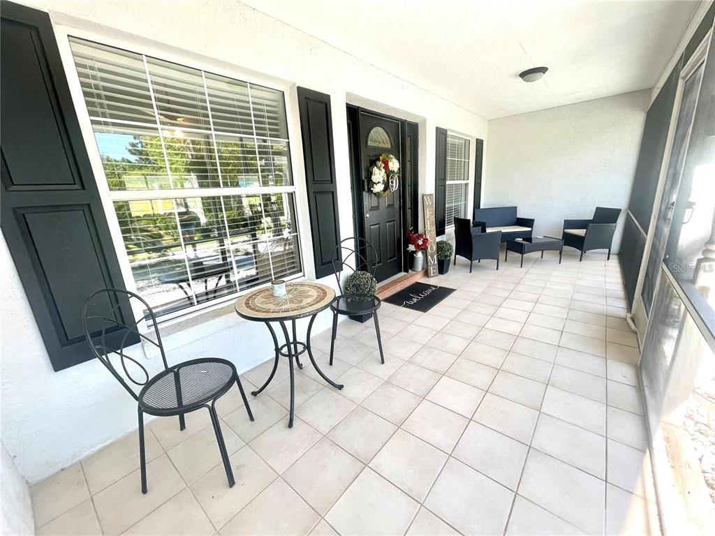 A covered patio features tiled flooring, black outdoor furniture, and a front door with shutters — 4353 W PINE RIDGE BOULEVARD, BEVERLY HILLS, FL