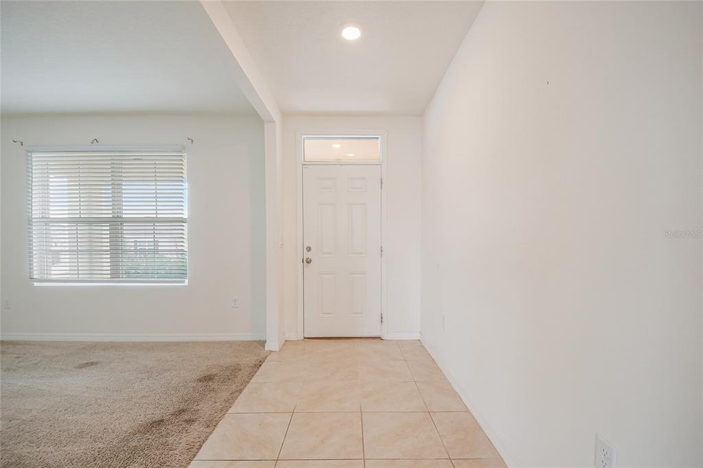 A carpeted room with white walls sits adjacent to a tiled hallway and living area — 2340 CANYON OAK DRIVE, DAVENPORT, FL