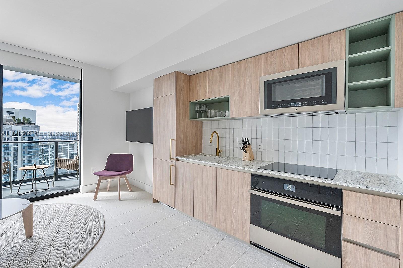 A modern kitchen features light wood cabinetry, white tile backsplash, and a balcony with city views — 159 NE 6th St # 2903, Miami FL 33132, MIAMI, FL