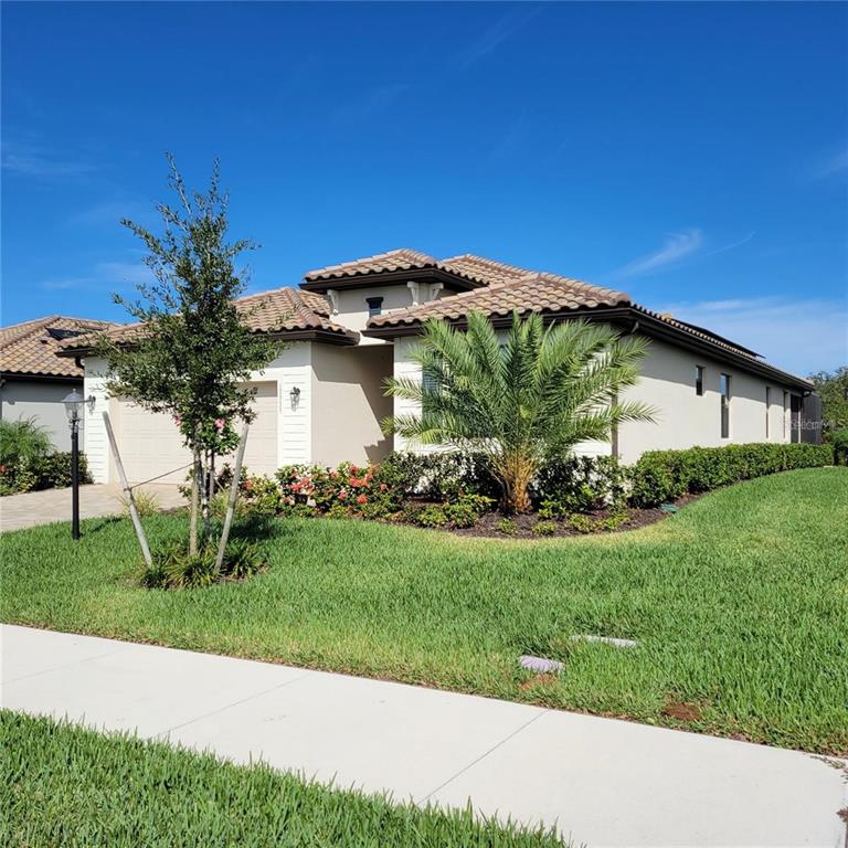 A single-story house with a tiled roof, beige stucco exterior, and a manicured front lawn — 17335 BLUE RIDGE PLACE, BRADENTON, FL