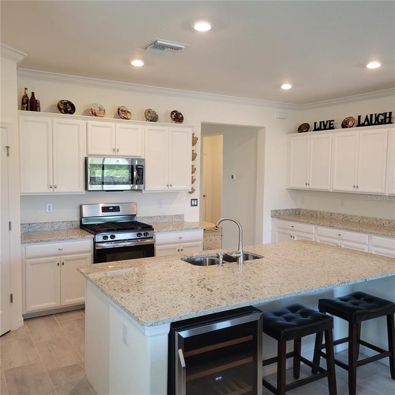 A kitchen features white cabinets, granite countertops, a center island with seating, and stainless appliances — 17335 BLUE RIDGE PLACE, BRADENTON, FL