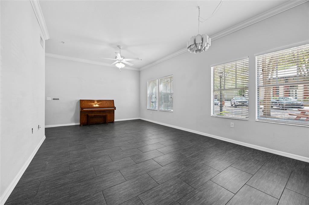 A spacious living room features dark tile flooring, a ceiling fan, and an upright piano — 5141 SW 91ST WAY UNIT I-102, GAINESVILLE, FL