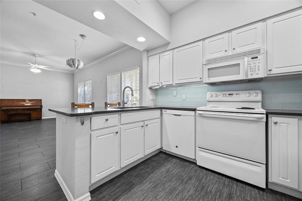 A kitchen with white cabinets, white appliances, and dark wood-look flooring opens to a living area — 5141 SW 91ST WAY UNIT I-102, GAINESVILLE, FL