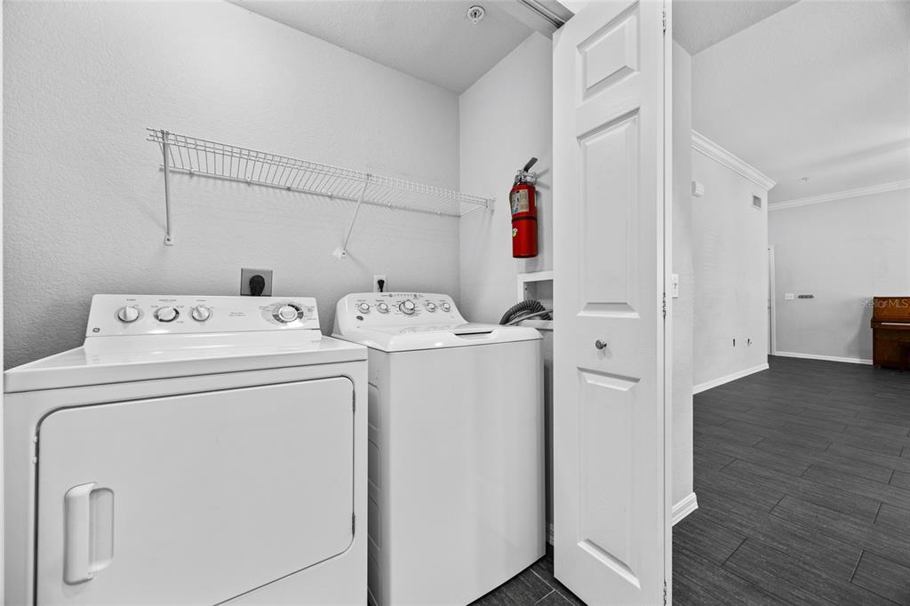 A laundry closet contains a white washer and dryer beneath a wire storage shelf — 5141 SW 91ST WAY UNIT I-102, GAINESVILLE, FL