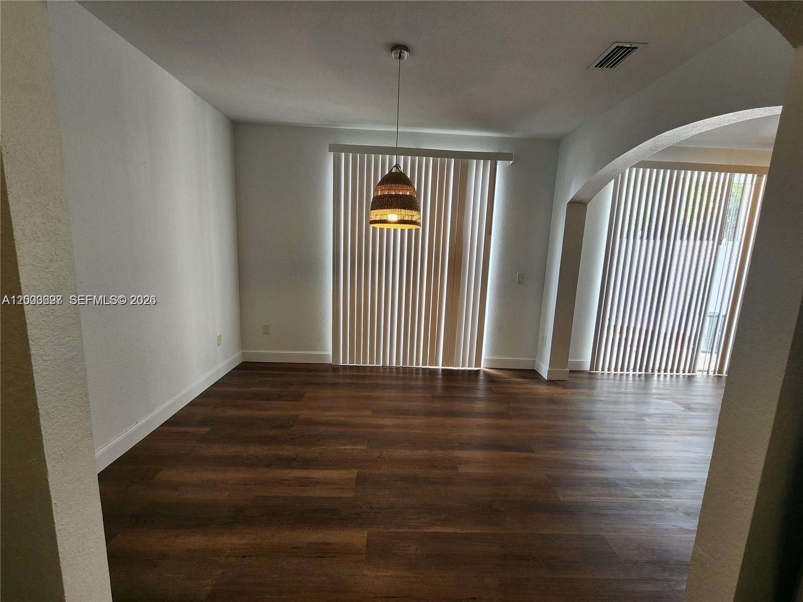 An empty dining area features dark wood-look flooring, white walls, and a woven pendant light — 15798 SW 40th St # 72, Miramar FL 33027, MIRAMAR, FL