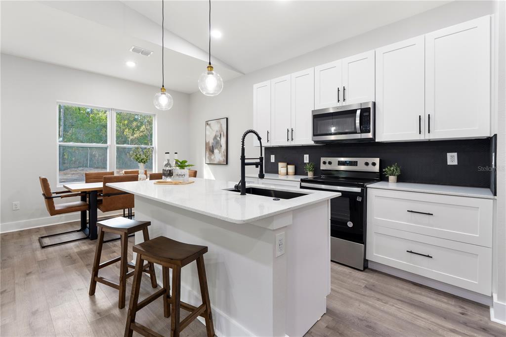A modern kitchen features white cabinets, a central island with a sink, and wood flooring — 12412 SW 98TH STREET, DUNNELLON, FL