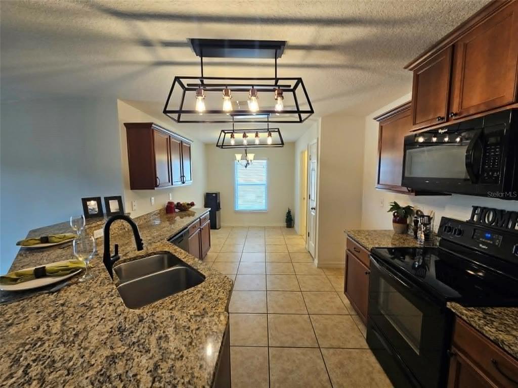 A kitchen features granite countertops, dark wood cabinets, black appliances, and two rectangular pendant lights — 30939 WATER LILY DRIVE, BROOKSVILLE, FL