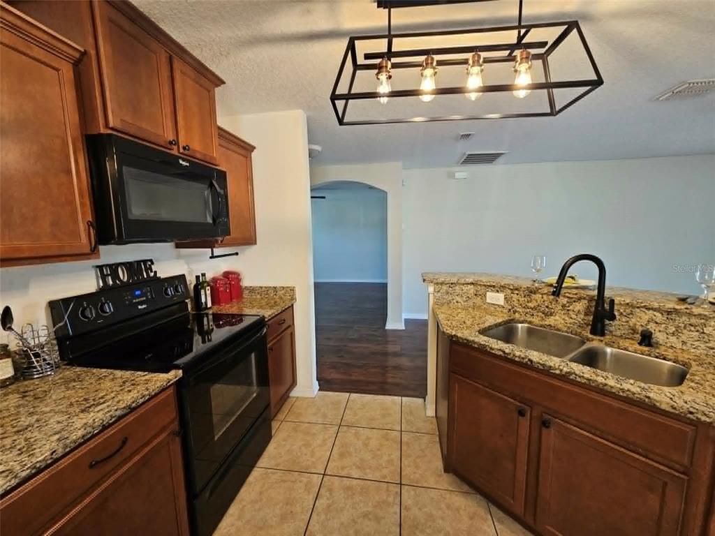 A kitchen features wood cabinets, granite countertops, a black stove, and a rectangular pendant light — 30939 WATER LILY DRIVE, BROOKSVILLE, FL
