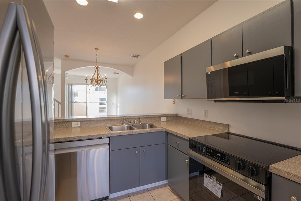 A kitchen with gray cabinets, stainless steel appliances, and a pass-through window to the dining area — 4712 HEMINGWAY HOUSE STREET, KISSIMMEE, FL