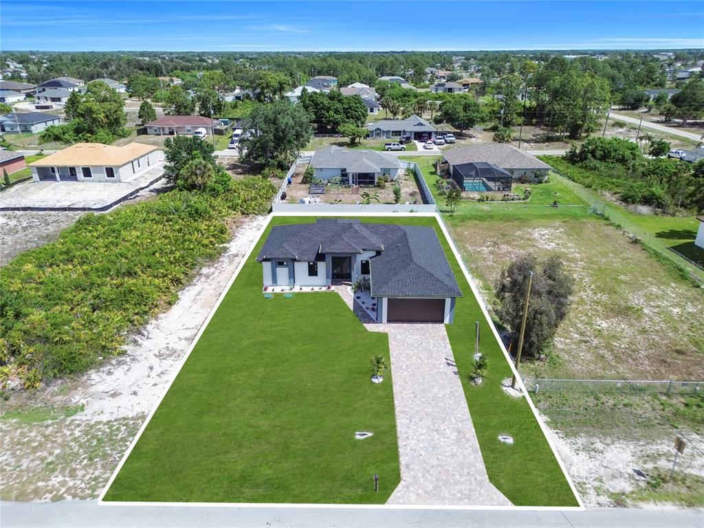 An aerial view shows a modern single-story house with a paved driveway and large lawn — 2606 40TH ST STREET, LEHIGH ACRES, FL