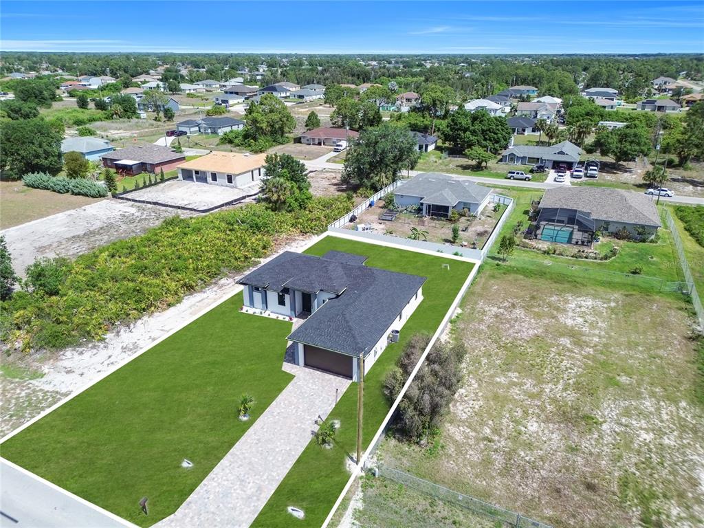 An aerial view shows a modern single-story house with a paved driveway and fenced yard — 2606 40TH ST STREET, LEHIGH ACRES, FL
