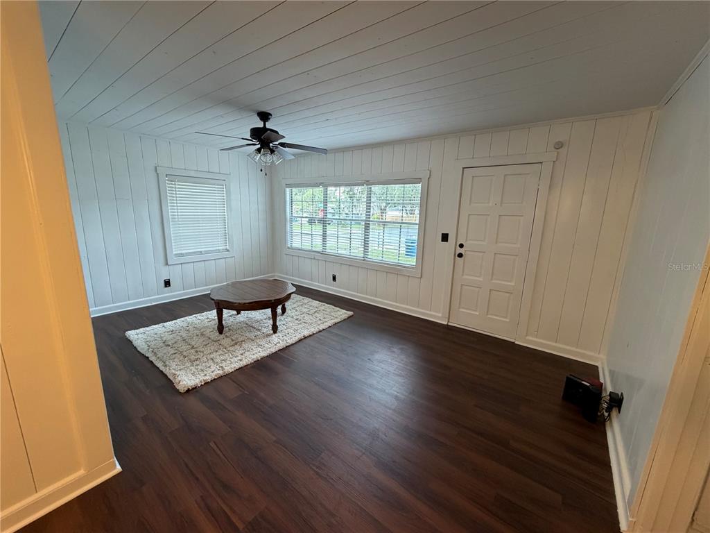 A living room features white wood-paneled walls, dark wood flooring, and a ceiling fan — 118 E PINE STREET, DAVENPORT, FL