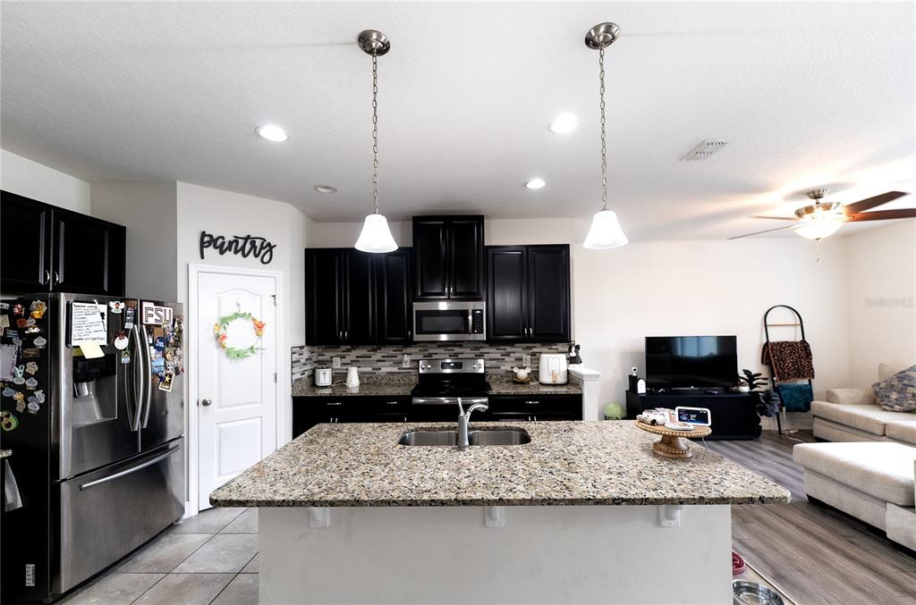 A kitchen features dark cabinets, granite countertops, a central island, and stainless steel appliances — 2749 PLEASANT CYPRESS CIRCLE, KISSIMMEE, FL
