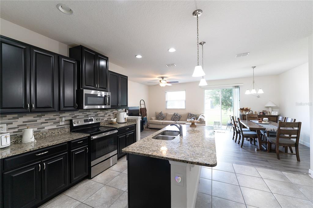 A kitchen with dark cabinets and granite countertops opens to a dining and living area — 2749 PLEASANT CYPRESS CIRCLE, KISSIMMEE, FL