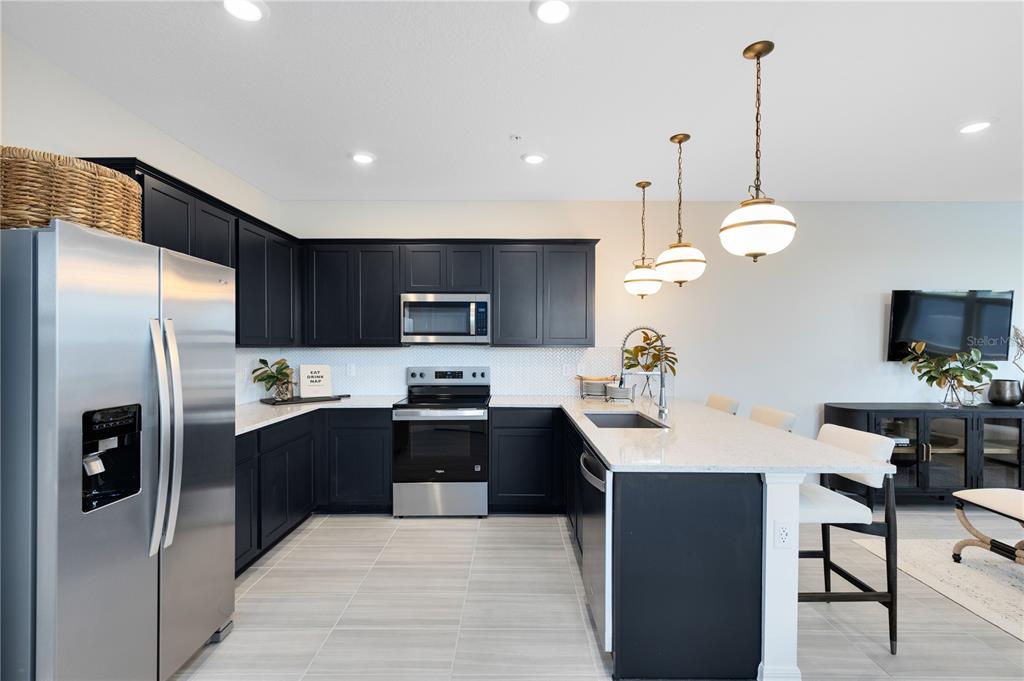 A modern kitchen features dark cabinets, stainless steel appliances, white countertops, and a breakfast island — 10106 HADLEY STREET, ORLANDO, FL