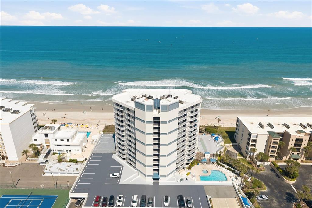 An aerial view of a high-rise beachfront condominium building with a pool and parking lot — 5207 S ATLANTIC AVENUE UNIT 1025, NEW SMYRNA BEACH, FL