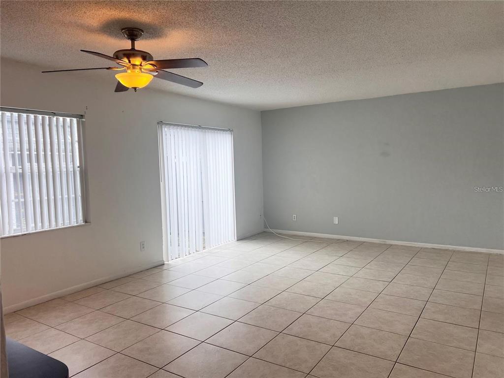 An empty living room features light-colored tile flooring, a ceiling fan, and vertical window blinds — 1000 S SEMORAN BOULEVARD UNIT 715, WINTER PARK, FL