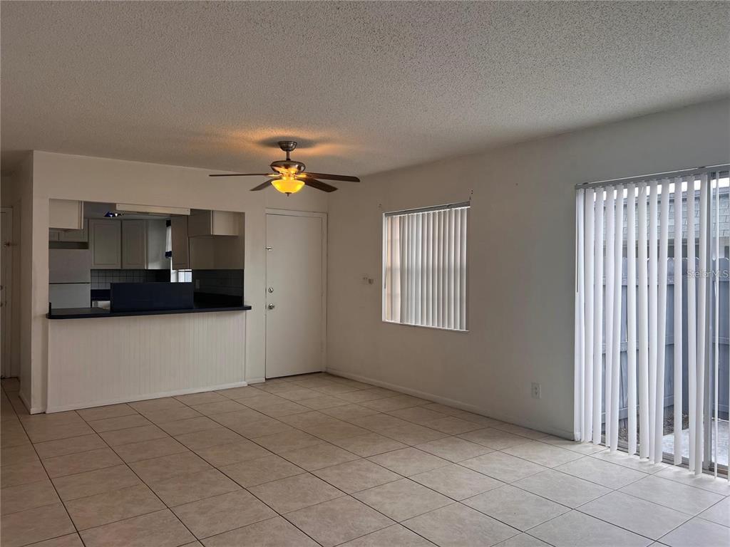 A living room with tile flooring, a ceiling fan, a kitchen pass-through, and sliding doors — 1000 S SEMORAN BOULEVARD UNIT 715, WINTER PARK, FL