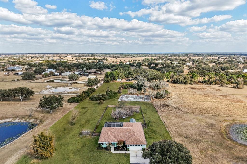 An aerial view shows a house with a pool cage surrounded by large, grassy fields — 803 BEL AIR STAR PARKWAY, SARASOTA, FL