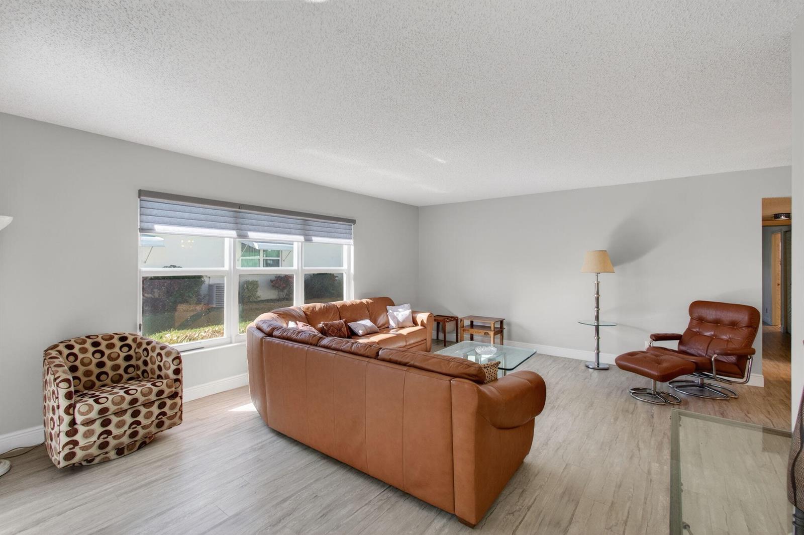 A living room features light wood-look flooring, a leather sectional, and a patterned accent chair — 5392 Lakefront Boulevard # A, Delray Beach FL 33484, DELRAY BEACH, FL