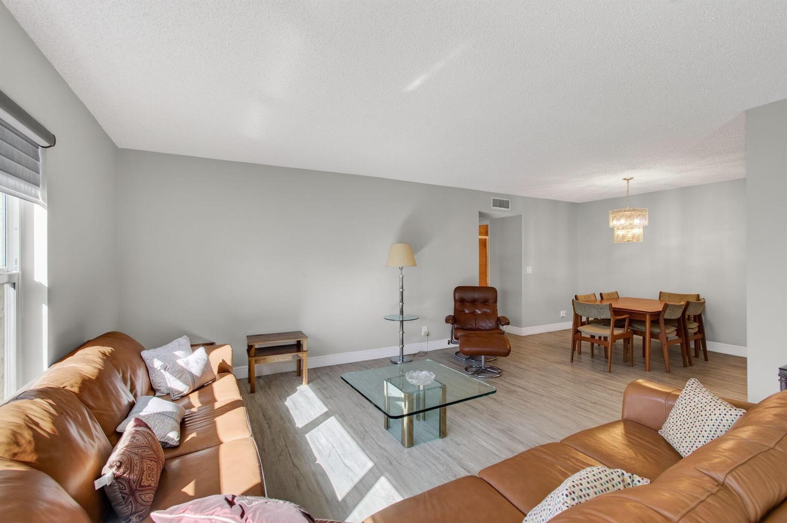 A living room with leather sofas, a glass coffee table, and an adjacent dining area — 5392 Lakefront Boulevard # A, Delray Beach FL 33484, DELRAY BEACH, FL