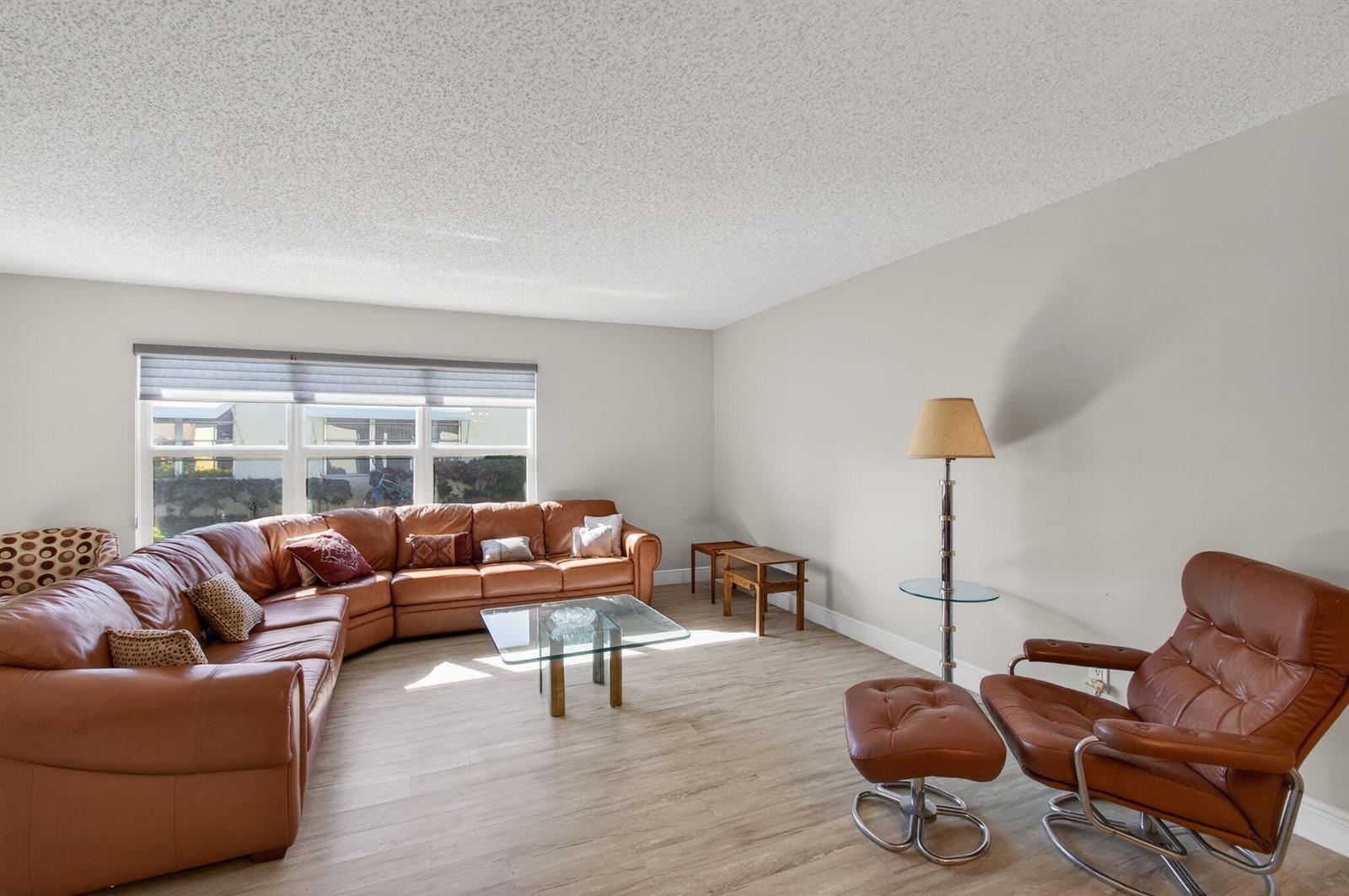A living room features a large leather sectional, a matching armchair with ottoman, and flooring — 5392 Lakefront Boulevard # A, Delray Beach FL 33484, DELRAY BEACH, FL