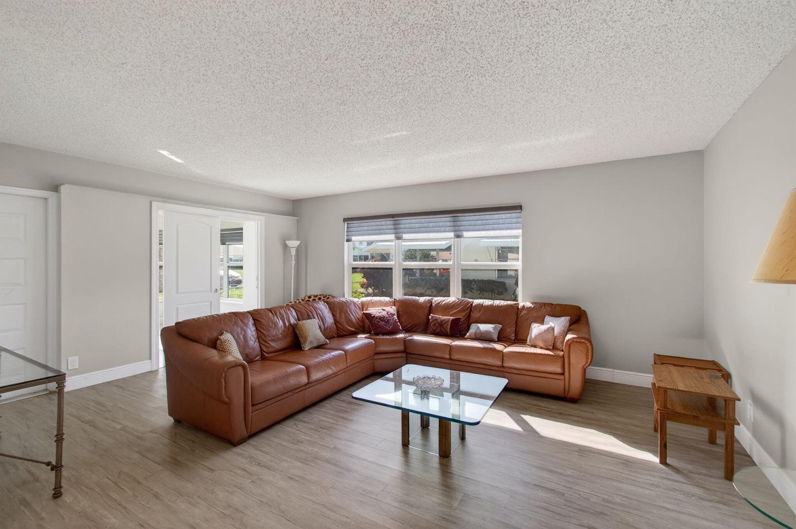 A living room features a large brown leather sectional, glass coffee table, and wood flooring — 5392 Lakefront Boulevard # A, Delray Beach FL 33484, DELRAY BEACH, FL