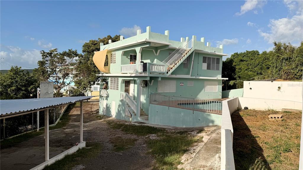 A three-story light green house features an outdoor staircase, balconies, and a swimming pool — 24 CALLE CORAL PLAYA SANTA, GUANICA, PR