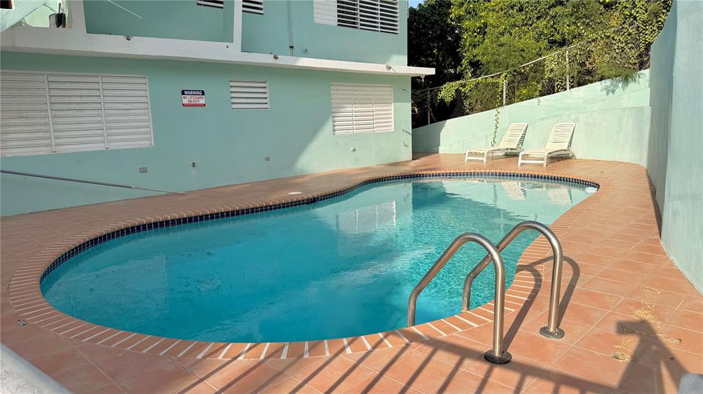 An outdoor swimming pool with a metal ladder sits on a tiled patio beside a building — 24 CALLE CORAL PLAYA SANTA, GUANICA, PR