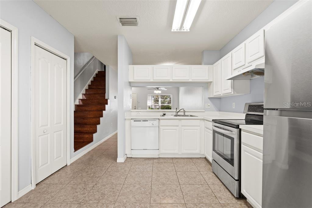 A kitchen with white cabinets, stainless steel appliances, tile flooring, and a staircase nearby — 2369 LAKE WOODBERRY CIRCLE, BRANDON, FL