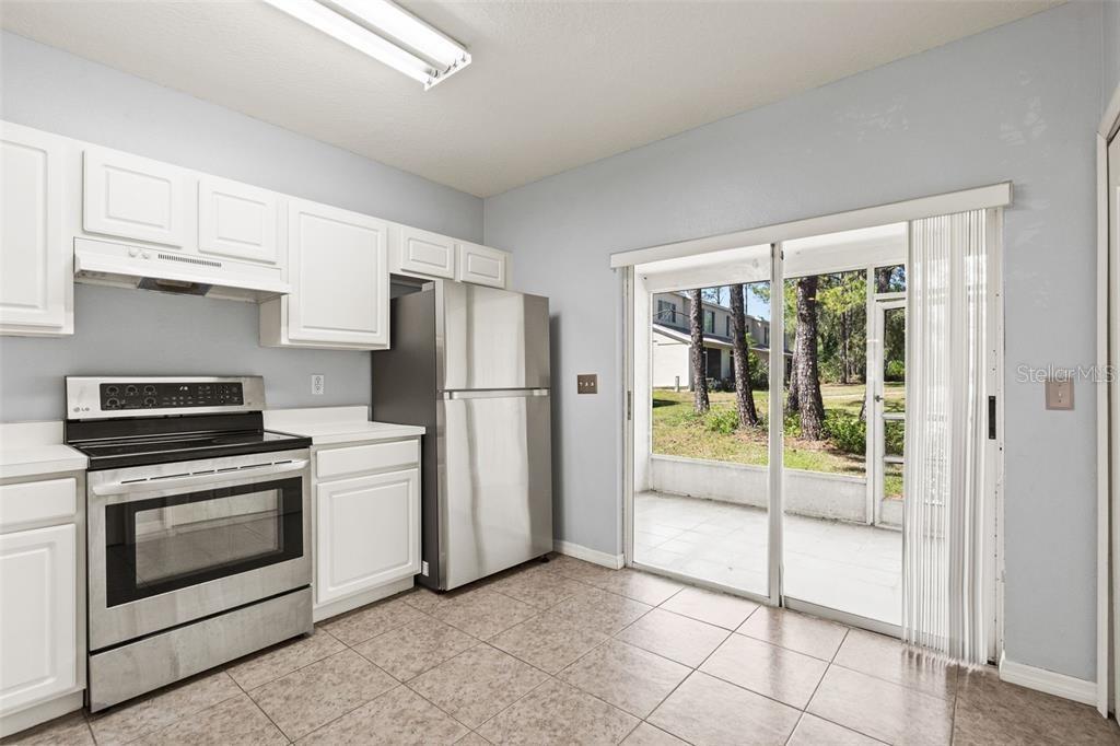 A kitchen with white cabinets, stainless steel appliances, tile flooring, and a sliding glass door — 2369 LAKE WOODBERRY CIRCLE, BRANDON, FL