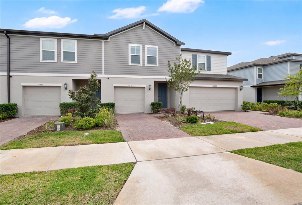 A row of three attached townhomes with gray siding, brick driveways, and two-car garages — 2026 CRAPE JASMINE LANE, ORLANDO, FL