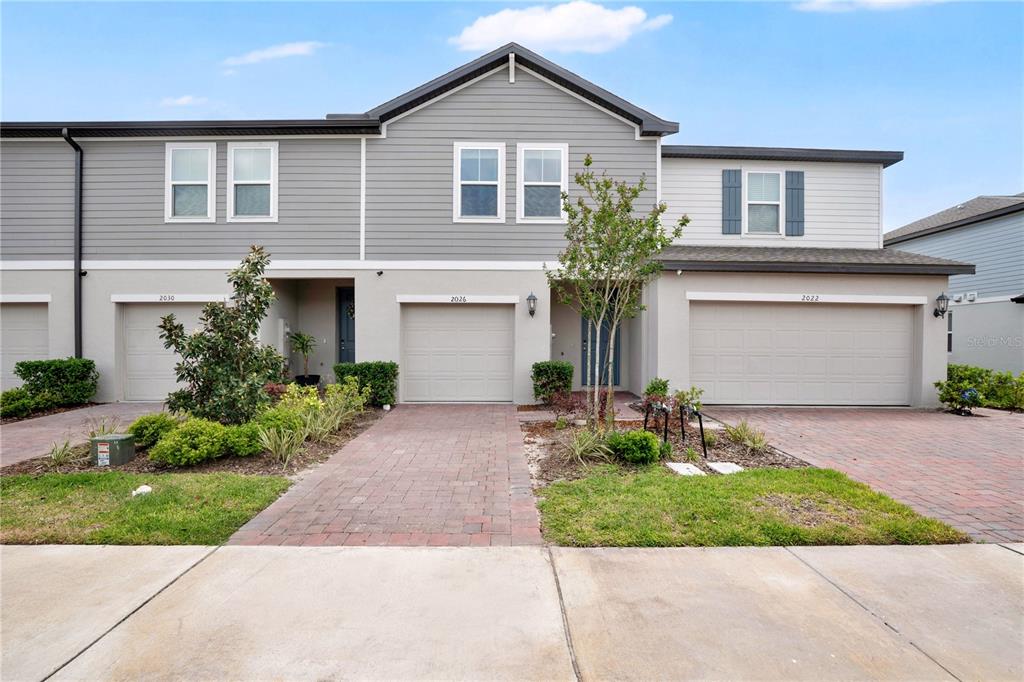 A row of three attached townhomes features gray siding, brick driveways, and two-car garages — 2026 CRAPE JASMINE LANE, ORLANDO, FL