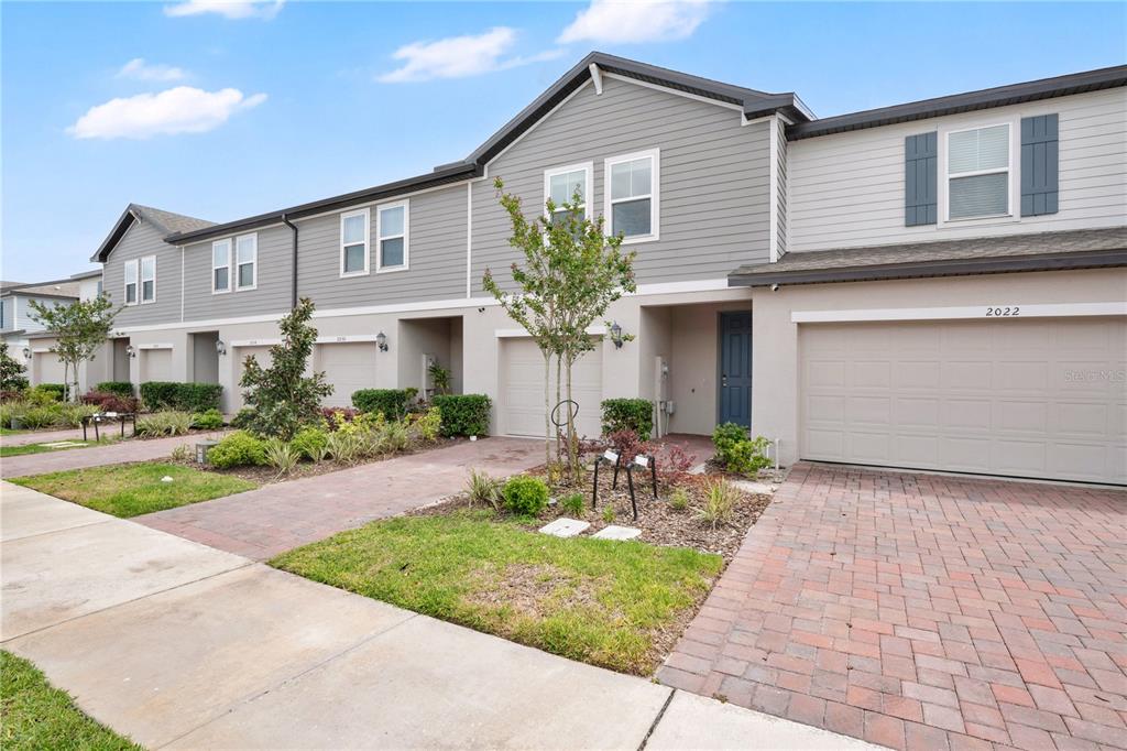 A row of multi-story townhomes with gray siding, stucco, and brick paver driveways — 2026 CRAPE JASMINE LANE, ORLANDO, FL