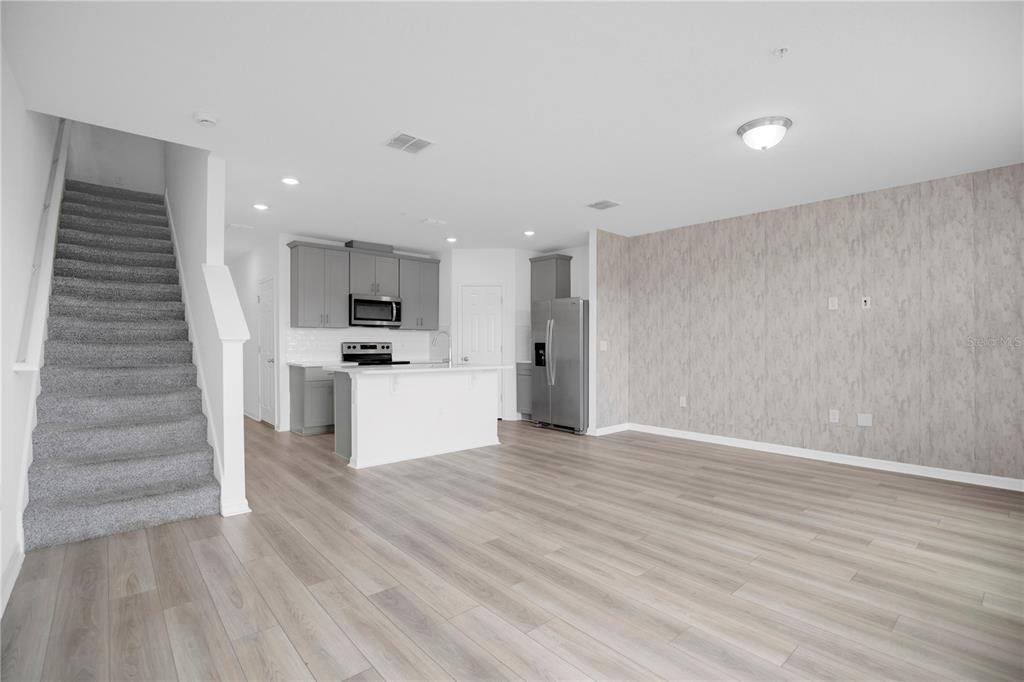 An open-concept living area features light wood-look flooring, a kitchen with gray cabinets, and stairs — 2026 CRAPE JASMINE LANE, ORLANDO, FL