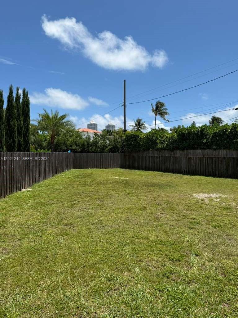 A grassy backyard is enclosed by a tall wooden fence under a blue sky — 5127 Alton Rd, Miami Beach FL 33140, MIAMI BEACH, FL