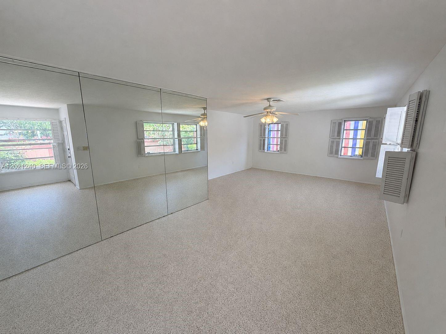 An empty room features beige carpeting, white walls, a ceiling fan, and mirrored closet doors — 5127 Alton Rd, Miami Beach FL 33140, MIAMI BEACH, FL