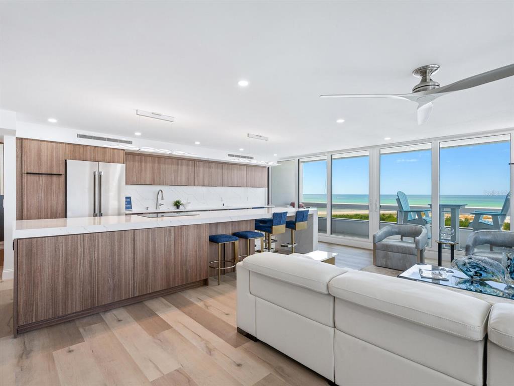A modern open-concept kitchen and living area features wood cabinetry, white countertops, and ocean views — 5400 OCEAN BOULEVARD UNIT 5-3, SARASOTA, FL