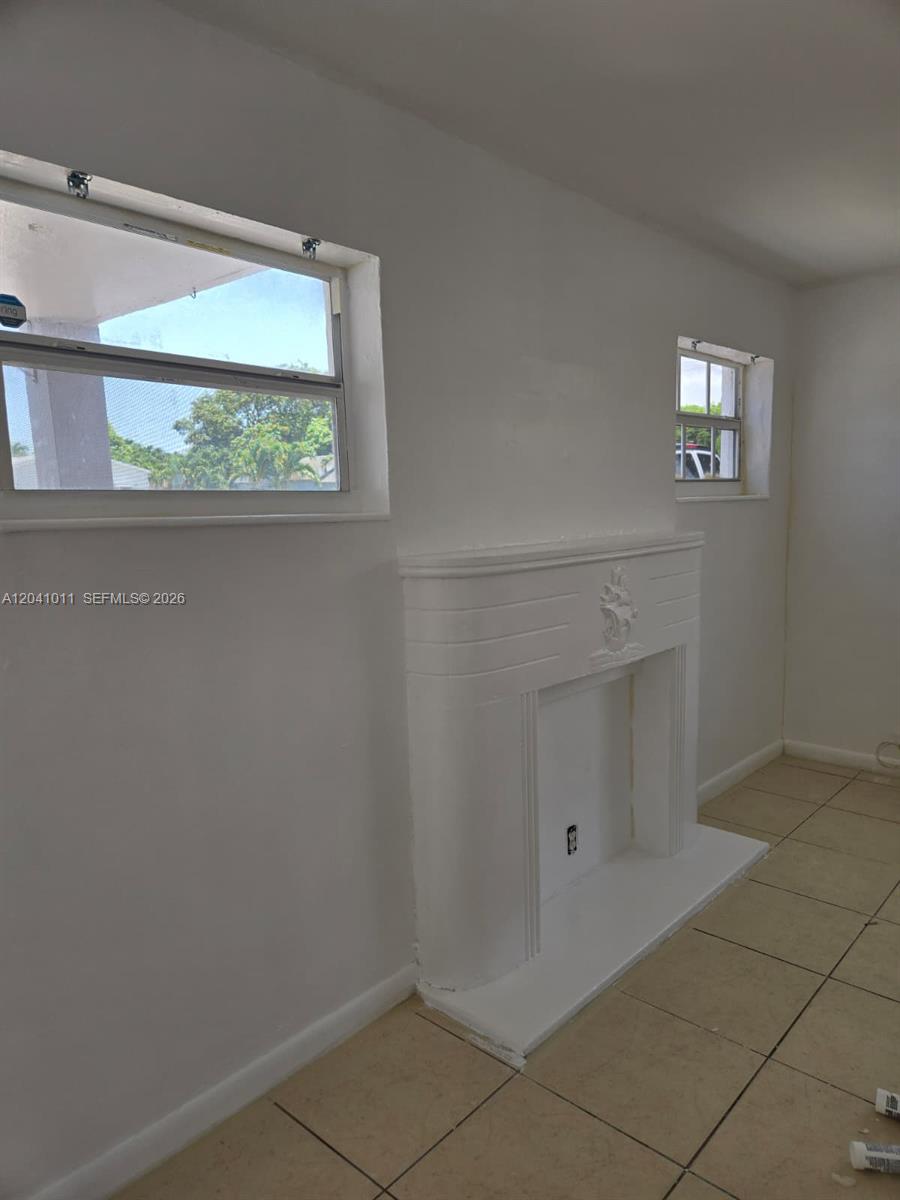 A room with white walls, tile flooring, two windows, and a decorative fireplace — 2325 Madison St # 1, Hollywood FL 33020, HOLLYWOOD, FL