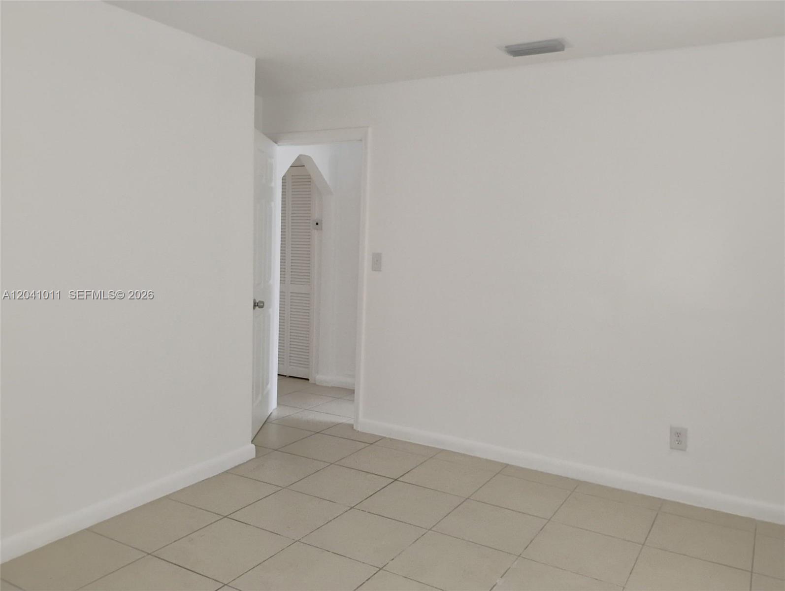 A room with white walls and light-colored tile flooring leads into a hallway with louvered doors — 2325 Madison St # 1, Hollywood FL 33020, HOLLYWOOD, FL