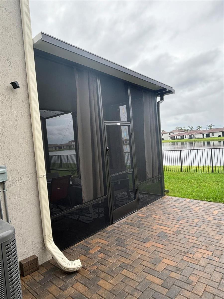 A screened-in patio with a paver floor overlooks a lake and neighboring houses — 5637 W Cerva Lane, Ave Maria FL 34142, AVE MARIA, FL