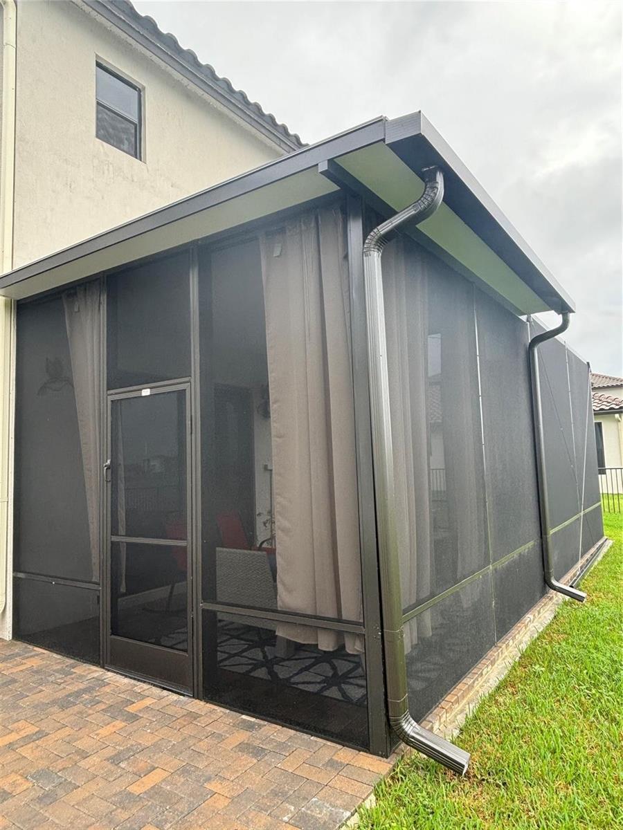 A screened-in patio with a dark metal frame, gutters, and curtains on a paved surface — 5637 W Cerva Lane, Ave Maria FL 34142, AVE MARIA, FL