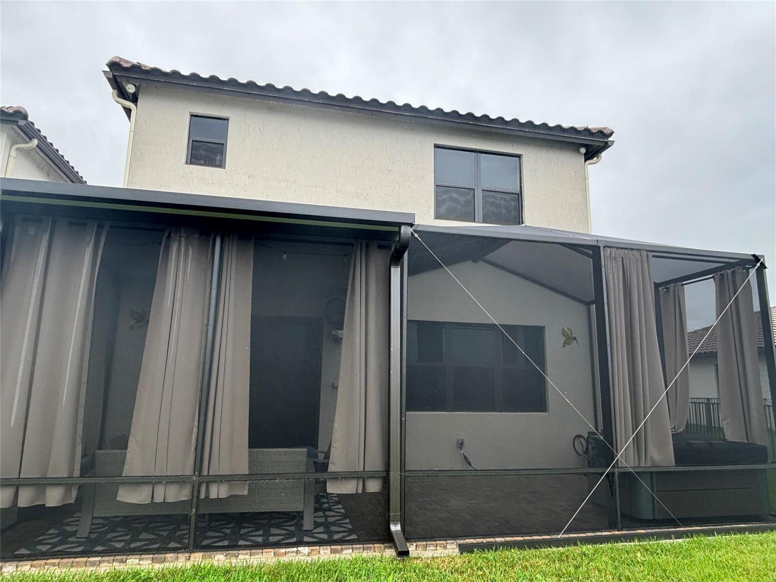 A two-story house exterior features a large screened-in patio with dark curtains and metal framing — 5637 W Cerva Lane, Ave Maria FL 34142, AVE MARIA, FL