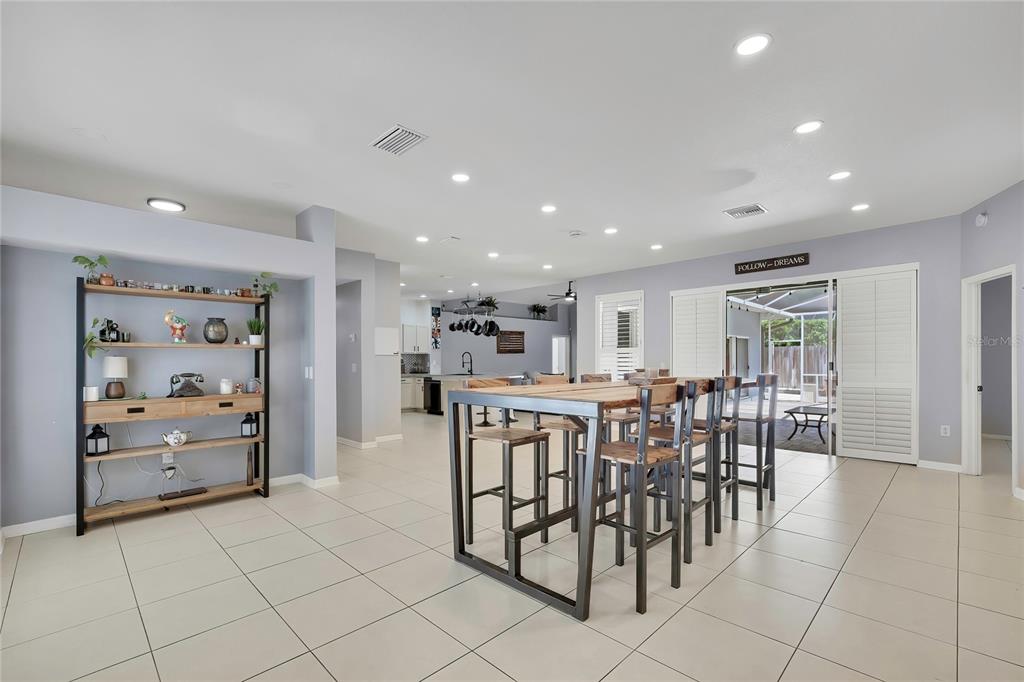 A spacious open-concept room features light tile floors, a tall wooden dining table, and shelving — 14105 MARLBERRY WAY, ODESSA, FL