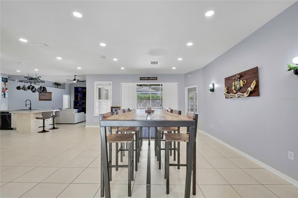 A spacious dining area features a long wooden table with metal stools on tiled floors — 14105 MARLBERRY WAY, ODESSA, FL